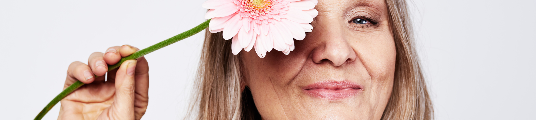 Older woman holding a pink flower infront of her face