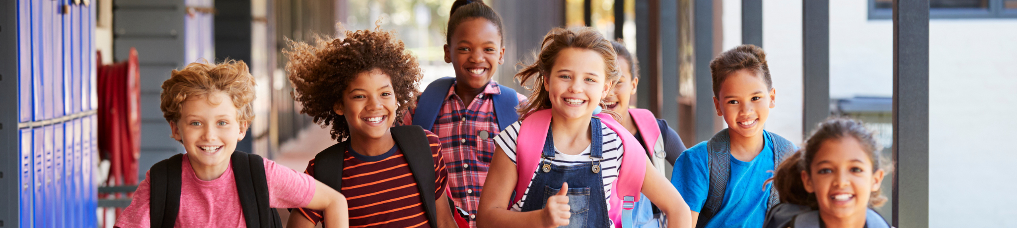 Group of older primary aged school children running through outdoor corridors of school